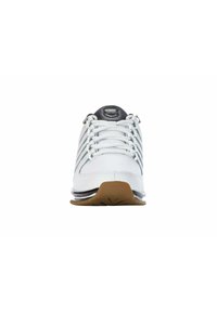 White athletic shoe with a smooth leather upper, white laces, and a cushioned sole featuring a gum rubber bottom. Accented with a black logo.