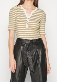 Randig, kortärmad topp i beige och vitt med V-ringning och tre-knapps knappslå. Matchad med högmidjade svarta läderbyxor.