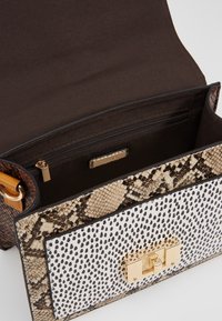 Rakennettu käsilaukku, jossa on sekoitus teksturoitua ruskeaa ja käärmeennahkakuosia, valkoisella, pilkullisella paneelilla ja kultaisilla varusteilla.