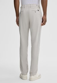 Pantaloni grigi chiari realizzati in un tessuto testurizzato, con una vestibilità dritta, tasche posteriori con bottoni, indossati con sneakers bianche.