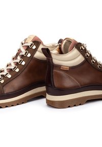 Bottes de randonnée en cuir marron avec des accents crème, finition texturée et quincaillerie en métal. Elles disposent d'une semelle en caoutchouc épaisse pour une meilleure traction.