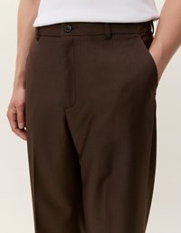 Rjav hlače s pinstripi in prilagojenim krojem, z gumbom spredaj in stranskima žepoma. Narejene so iz gladkega materiala z diskretno teksturo.