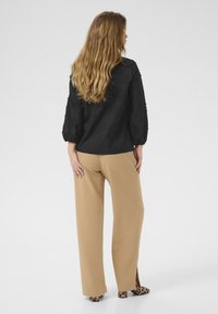 Schwarze, strukturierte Bluse mit Ballonärmeln, kombiniert mit hochgeschnittenen sandfarbenen Hosen mit seitlichen Schlitzen. Tiermuster-Absätze runden den Look ab.
