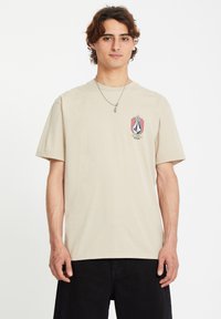 Beige cotton t-shirt with short sleeves, featuring a colorful graphic logo on the left chest and a crew neckline.