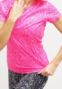 Camiseta deportiva rosa con un patrón texturizado, mangas cortas y un diseño ajustado. Combinada con leggings de diseño en blanco y negro.