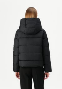 Casaco puffer preto com um grande capuz, design acolchoado e silhueta cropped. Apresenta mangas largas e uma textura lisa e mate.