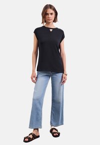 Černý top s krátkým rukávem a detaily v oblasti krku, kombinovaný s světle modrými širokými džíny a černými sandály s leopardím vzorem.