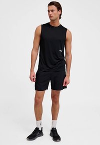 Czarna sportowa koszulka bez rękawów w parze z czarnymi szortami. Tkanina jest lekka, gładka. Noszona z czarnymi trampkami i białymi skarpetkami z czarnymi akcentami.