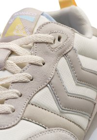 Beżowe i kremowe sneakersy z teksturowaną siateczką, skórzanymi akcentami i kontrastowym wzorem w zygzak. Posiadają kremowe sznurówki oraz kolorową metkę z logo.