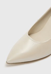 Μπαλαρίνα με μυτερή μύτη από υφή κρεμ δέρμα, με ρηχό κόψιμο, λεία εσωτερική επένδυση και λεπτή, επίπεδη σόλα.