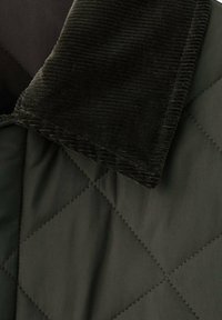 Giacca trapuntata verde scuro, con colletto in velluto a costine nero a contrasto. Tessuto liscio con motivo a rombi sul corpo.