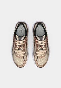 Chaussures de course légères avec un dessus en mesh beige, des accents marron et un col noir. Caractéristiques : lacets crème et semelle intérieure grise rembourrée.