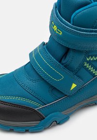 Botas de senderismo azules con acentos amarillos, fabricadas con materiales duraderos, con dos correas de velcro, superficie texturizada y suela de goma negra.