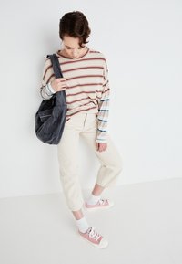 Langermet stripete skjorte i beige, rød og blå. Beige cropped bukser og rosa sneakers, kombinert med en grå lerret skulderveske.