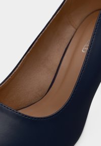 Γόβα από μπλε ναυτικό δέρμα με λείο φινίρισμα, στρογγυλεμένη μύτη και μπεζ εσωτερικό. Διαθέτει διακριτικές ραφές κατά μήκος της άνω άκρης.