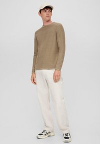  Lichtbruine lange mouwen shirt met een ronde hals, gecombineerd met witte recht gesneden jeans en zwart-witte sneakers, en een beige pet.