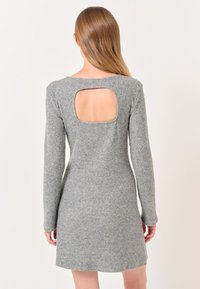 Robe en tricot grise avec des manches longues, une silhouette ajustée et une découpe rectangulaire dans le dos. Texture douce et détail de conception côtelée.