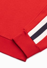 Sudadera roja con puños acanalados que presenta un diseño de rayas en blanco y azul marino en la manga. Textura suave, corte clásico.