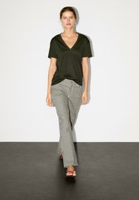 Czarny t-shirt z dekoltem w serek połączony z szerokimi spodniami w paski. Model nosi różowe sandały. Gładka faktura materiału, luźny krój i casualowy styl.