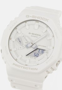 White G-SHOCK watch with a digital display, analog hands, textured silicone strap, and silver accents; shows time, date, and various modes.