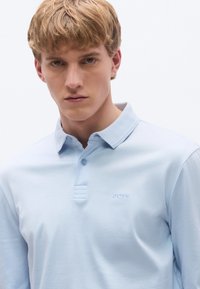 Ανοιχτό μπλε πόλο από βαμβάκι, με γιακά, σειρά κουμπιών και κεντημένο λογότυπο "BOSS" στο αριστερό στήθος. Ομαλή υφή.