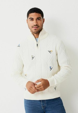 Gebreide trui in crème met een kwart ritssluiting, ruitpatroon en geborduurde skiërsmotieven in blauw, groen, geel en oranje.