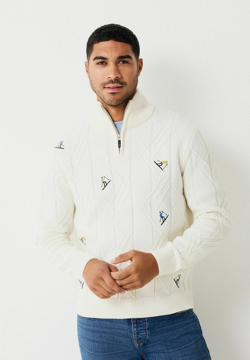 Adīts džemperis krēmkrāsā ar ceturtdaļas rāvējslēdzēju, dimanta rakstu un izšūtām slēpotāju motīviem zilos, zaļos, dzeltenos un oranžos toņos.