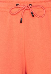Korallfärgade joggingshorts i mjukt tyg, med resårmidja och svarta aglets. Ytan har en slät textur.