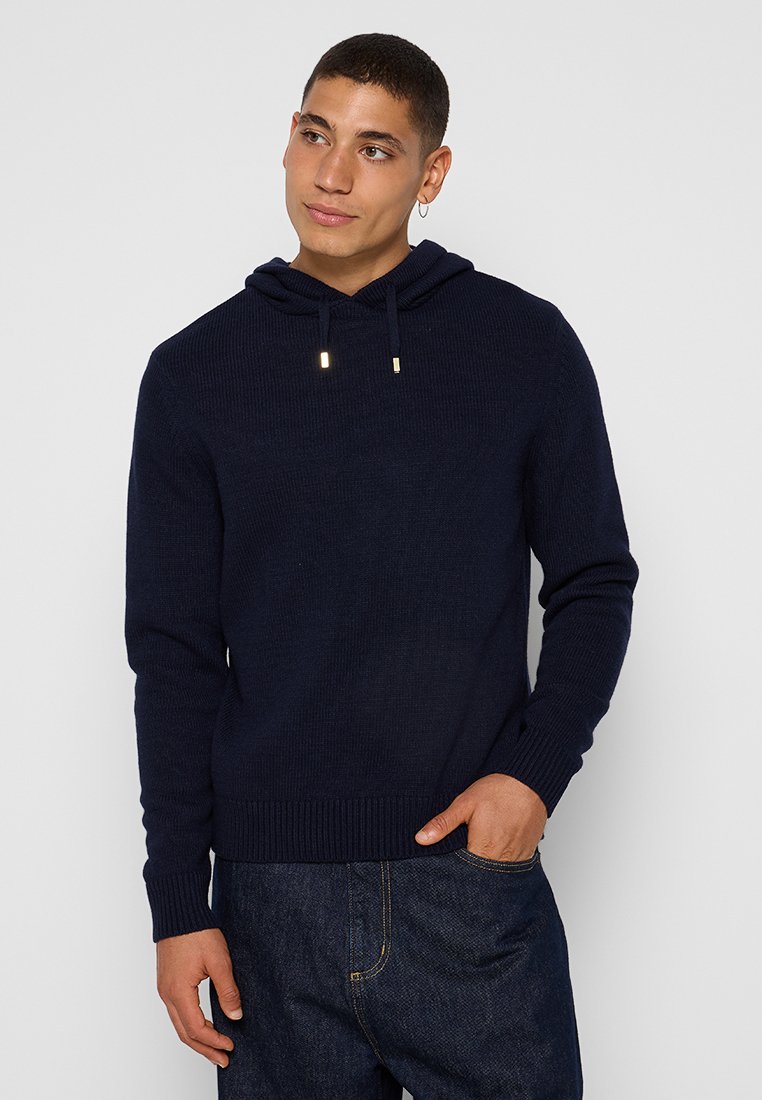 Dunkelblaues Strick-Hoodie mit Kordelzug, gerippten Bündchen und Saum. Getragen über dunklen Jeans, mit einem einfachen und klassischen Design.