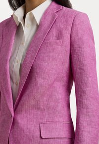 Skräddarsydd kavaj i strukturerad rosa herringbone-tyg, med notch-revers, enfaldig bröstficka och en strukturerad passform över en vit skjorta.
