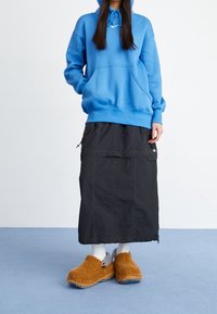 Blå hoodie med framficka, kombinerad med en svart lång kjol med sidofickor. Bruna fluffiga clogs med grå detaljer och vita strumpor.