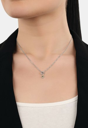 Collana d'argento con una delicata catena, caratterizzata da un pendente a forma di cuore e una piccola pietra verde. Design minimalista, texture liscia.