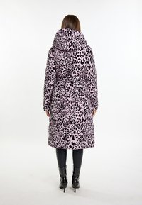 Gepolsterter Mantel in Hellrosa mit schwarzem Leopardenmuster, mit Kapuze und Bindegürtel, kombiniert mit schwarzen engen Hosen und glänzenden Ankle Boots.