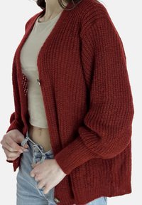 Gebreid vest in roestrood met een losse pasvorm, open voorkant, geribbeld patroon, lange mouwen en knoopdetail aan de zoom.