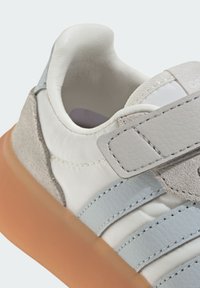Baskets blanches avec des accents en cuir et en daim gris, tige en textile, semelle en caoutchouc orange et une sangle Velcro.