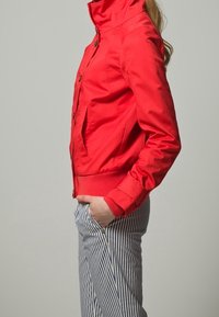 Czerwona, lekka kurtka z wysokim kołnierzem, z guzikami z przodu i prążkowanymi rękawami, zestawiona z niebieskimi i białymi spodniami w paski. Gładka tekstura, dopasowany krój.