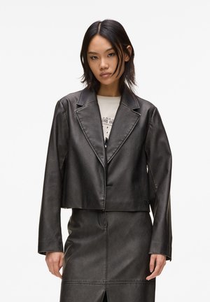 Černý cropped faux kůžový blazer s klopami, zapínáním na jeden knoflík a dlouhými rukávy, stylizovaný přes odpovídající sukni.