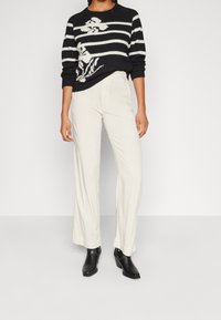 Maglione a righe bianche e nere con un motivo floreale, abbinato a pantaloni larghi color crema e stivali neri alla caviglia.