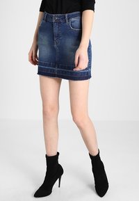 Jupe en denim bleu foncé, avec un ourlet effiloché et un léger délavage. Stylisée avec une ceinture classique et des poches avant.