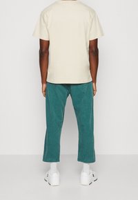 Krémové bavlněné tričko s krátkým rukávem v kombinaci s tyrkysovými manšestrovými kalhotami širokého střihu. Obsahuje bílé tenisky a bílé ponožky.