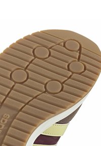 Sulan på en sko med ett spårigt, texturerat mönster i ljusbrun gummi, med cirkulära gripytor och en vit mellansula.