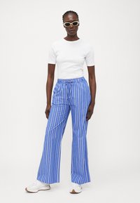 Blue and white striped wide-leg pants with a drawstring waist, paired with a fitted white short-sleeve top and white sneakers.