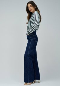 Jean taille haute à jambes larges en denim foncé, associé à un chemisier à manches longues rayé en vert et crème. Présente un design classique à cinq poches.