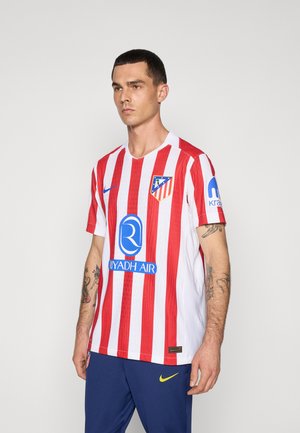 Atletico Madrid trøje med røde og hvide lodrette striber, korte ærmer, V-halskrave, med blå sponsortekst og logo på brystet.