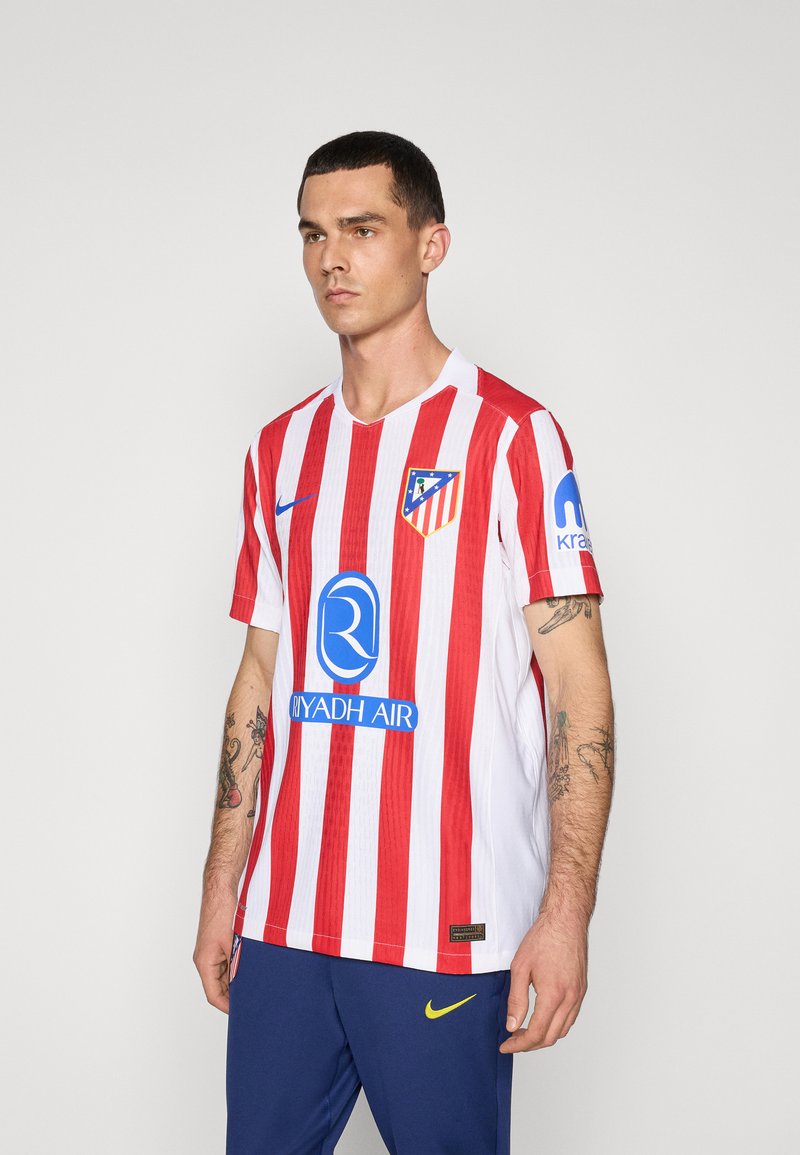 Atletico Madridin pelipaita, jossa on punaiset ja valkoiset pystysuorat raidat, lyhyet hihat, V-pääntie, ja sininen sponsoriteksti ja logo rinnassa.