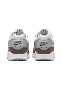 Sneakers Nike Air w kolorze szarym, brązowym i białym. Posiadają wyściełany kołnierz, paskowany podszewkę oraz akcenty logo na pięcie. Gumowa podeszwa.