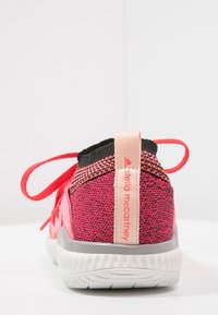 Červené a růžové sportovní boty s texturovaným pleteným svrškem, černými akcenty a šedou podrážkou. Mají štítek s logem na patě a kontrastní tkaničky.