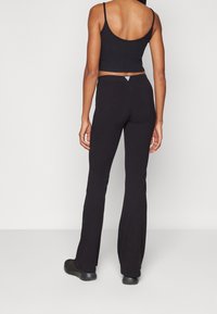 Czarny prążkowany crop top w połączeniu z czarnymi spodniami dzwonami. Materiał wydaje się miękki i elastyczny, z minimalnymi elementami metalowymi i małym detalem z logo.