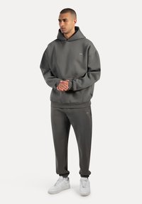 Felpa grigia con cappuccio e pantaloni coordinati in tessuto morbido. Presenta una tasca a marsupio, polsini a coste e sneakers bianche.