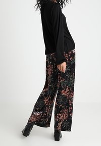 Czarna bluzka z długim rękawem w połączeniu z luźnymi czarnymi spodniami w kwiaty z różowymi i zielonymi wzorami. Tkanina o fakturze i szerokie nogawki.